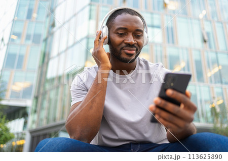 Music song concept. Good start day. Happy African American man listening modern hit on street in city. Person guy wearing headphones enjoy listening favorite music on phone. People lifestyle joy 113625890