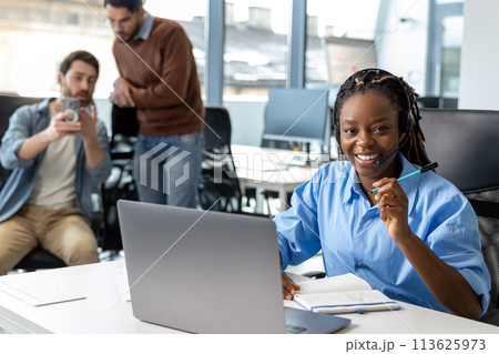 Attractive dark skinned woman in headset working on laptop Attractive dark skinned woman in headset working on laptop 113625973