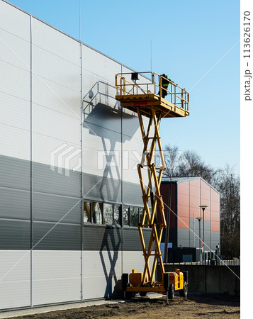 High elevated yellow self propelled scissor lift platform with worker for building wall inspection 113626170