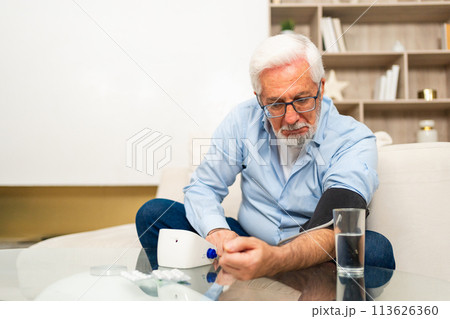 Hypertension problem in senior age. Old man measuring blood pressure with tonometer at home. Senior man have health problem making self checkup. Headache treatment of hypertension hypotension 113626360