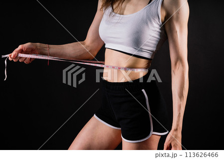 Athletic slim woman measuring her waist by measure tape after a diet over dark yellow background Athletic slim woman measuring her waist by measure tape after a diet over dark yellow background 113626466
