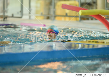 A child in a silicone cap and glasses learns to swim in the pool 113628586