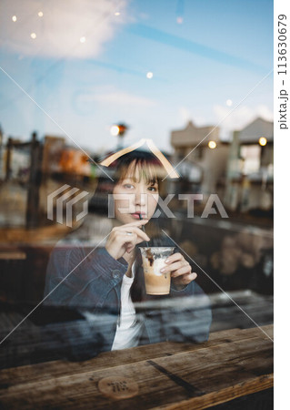 ガラス越しから撮るカフェで飲み物を飲んでいる女性 ガラス越しから撮るカフェで飲み物を飲んでいる女性 113630679