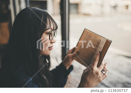 カフェの窓際の席でコーヒーを飲みながら休日に読書する若い女性 カフェの窓際の席でコーヒーを飲みながら休日に読書する若い女性 113630737