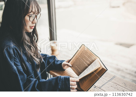 カフェの窓際の席でコーヒーを飲みながら休日に読書する若い女性 カフェの窓際の席でコーヒーを飲みながら休日に読書する若い女性 113630742
