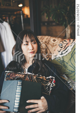 カフェの窓際の席でコーヒーを飲みながら休日に読書する若い女性 113630752