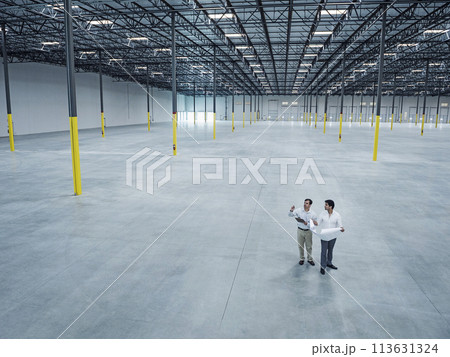 Architects with blueprint talking in empty warehouse 113631324