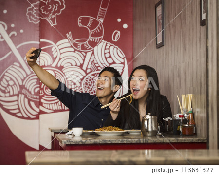 Chinese couple posing for cell phone selfie in restaurant Chinese couple posing for cell phone selfie in restaurant 113631327