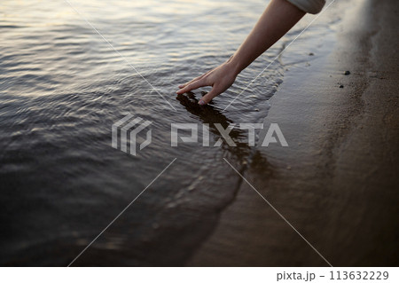 Close-up of woman touching water in river at sunset 113632229