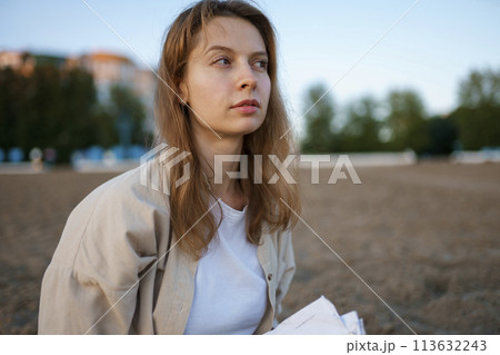 Portrait of thoughtful woman with book on beach 113632243
