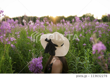 Side view of young woman looking at flowers on meadow 113632278