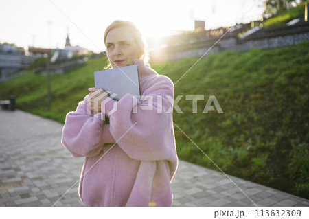 Woman embracing laptop while standing outdoors at sunrise Woman embracing laptop while standing outdoors at sunrise 113632309