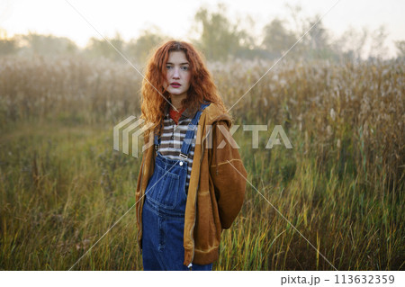 Portrait of young woman standing in field at dawn Portrait of young woman standing in field at dawn 113632359