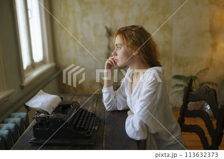 Side view of woman using vintage typewriter at home Side view of woman using vintage typewriter at home 113632373