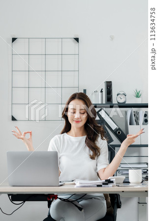 Businesswoman closes her eyes and meditates, practicing mindfulness to maintain balance during a busy workday. 113634758