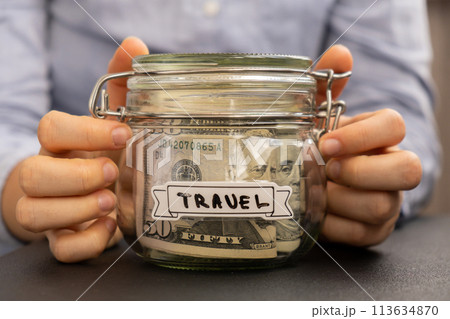 Unrecognizable woman holding Saving Money In Glass Jar filled with Dollars banknotes. TRAVEL transcription in front of jar. Managing personal finances extra income for future insecurity Unrecognizable woman holding Saving Money In Glass Jar filled with Dollars banknotes. TRAVEL transcription in front of jar. Managing personal finances extra income for future insecurity 113634870