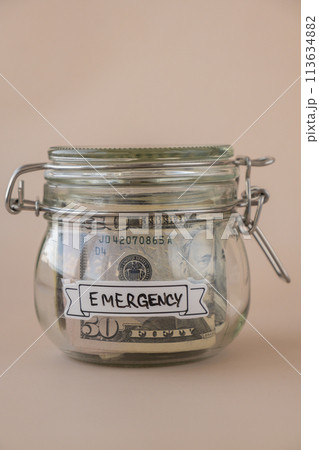 Saving Money In Glass Jar filled with Dollars banknotes. EMERGENCY transcription in front of jar. Managing personal finances extra income for future insecurity Saving Money In Glass Jar filled with Dollars banknotes. EMERGENCY transcription in front of jar. Managing personal finances extra income for future insecurity 113634882