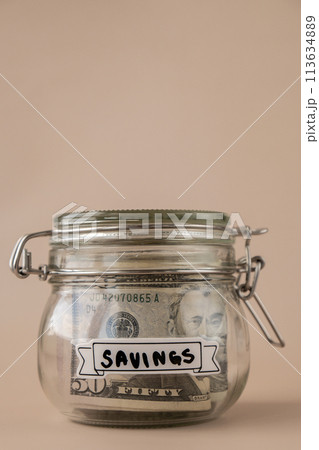 Saving Money In Glass Jar filled with Dollars banknotes. SAVINGS transcription in front of jar. Managing personal finances extra income for future insecurity 113634889