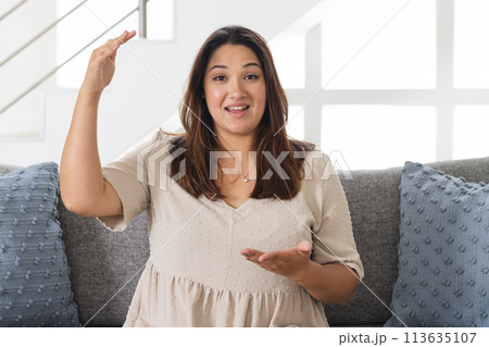 Young biracial woman gestures animatedly on a sofa at home on a video call 113635107