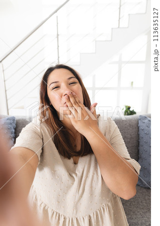 Young biracial woman takes a selfie at home on a video call, blowing a kiss Young biracial woman takes a selfie at home on a video call, blowing a kiss 113635127