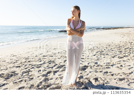 Young Caucasian woman stands on a sunny beach, with copy space 113635354