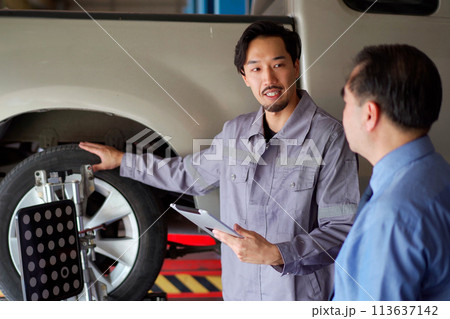 Asian car technician or repairman inspecting the suspension system under the car. Repairman working in garage. Garage manager talking or explaining about the progress of repairing client's vehicle. Asian car technician or repairman inspecting the suspension system under the car. Repairman working in garage. Garage manager talking or explaining about the progress of repairing client's vehicle. 113637142