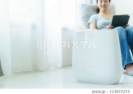 Happy Asian young woman turning on high efficiency air purifier while staying and relaxing in the living room. Woman using air purifier in her house. 113637253