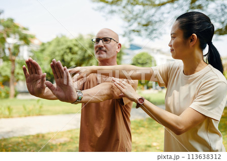 Tai chi instructor explaining g client how to keep arms straight when doing exercise 113638312