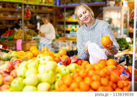 Positive female shopper looking for sweet oranges in supermarket 113639030