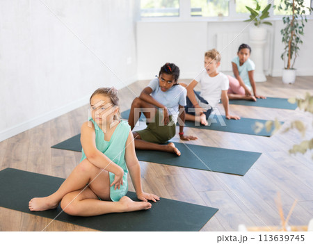 In sport studio with group of friends, girl perform Lord of Fishes asana, Ardha Matsyendrasana 113639745
