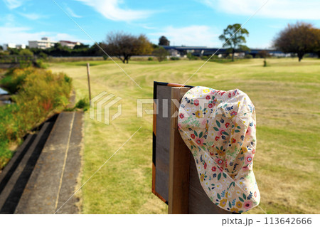 晴れた公園内にある川の利用注意看板に、忘れ物の女性用帽子が掛けてある 晴れた公園内にある川の利用注意看板に、忘れ物の女性用帽子が掛けてある 113642666