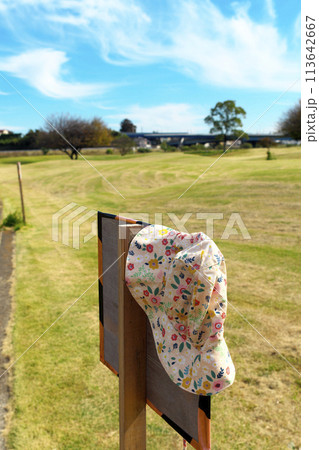 晴れた公園内にある川の利用注意看板に、忘れ物の女性用帽子が掛けてある 晴れた公園内にある川の利用注意看板に、忘れ物の女性用帽子が掛けてある 113642667