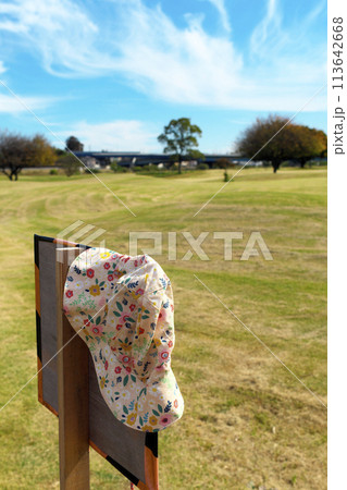 晴れた公園内にある川の利用注意看板に、忘れ物の女性用帽子が掛けてある 113642668