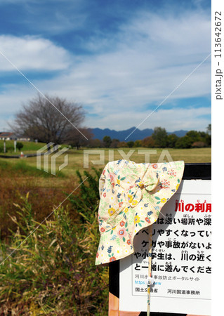 晴れた公園内にある川の利用注意看板に、忘れ物の女性用帽子が掛けてある 晴れた公園内にある川の利用注意看板に、忘れ物の女性用帽子が掛けてある 113642672