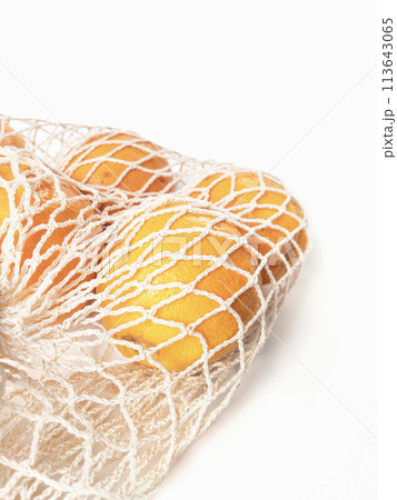 Fresh unpeeled oranges placed in reusable white mesh bag 113643065