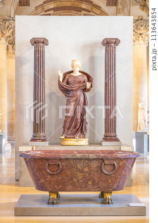 Praying Woman between Two Ionic Columns. A woman in a draped dress stands praying between two Ionic columns inside the Louvre Museum, exhibiting classical antiquity. Paris, France Praying Woman between Two Ionic Columns. A woman in a draped dress stands praying between two Ionic columns inside the Louvre Museum, exhibiting classical antiquity. Paris, France 113643854