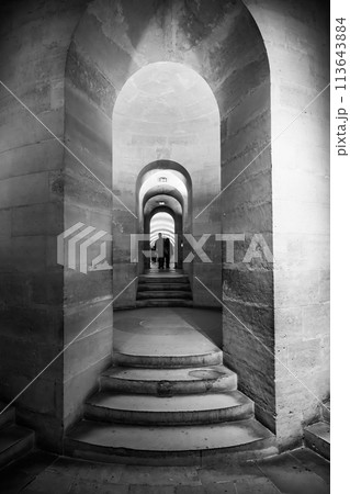 Stone arches lead down to the crypt of the Pantheon in Paris, with visitors visible in the distance. Paris, France 113643884