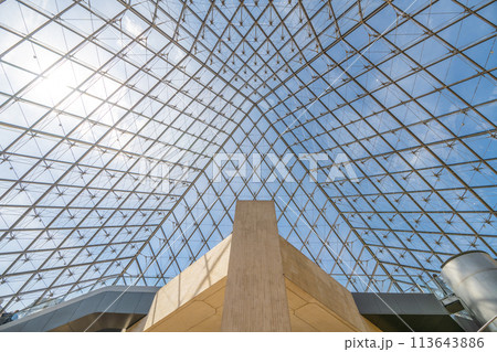 The geometric glass panels of the Louvre Pyramid, viewed from beneath against a clear blue sky in Paris, with interior structures visible. France 113643886