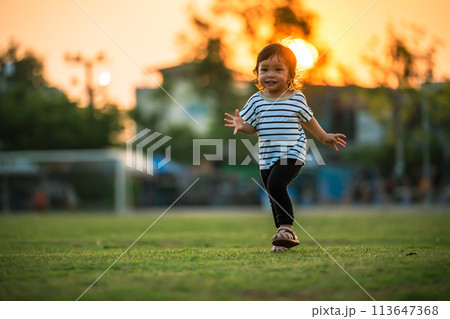 happy toddler girl running on grass field in park at sunset 113647368