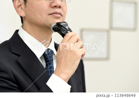 スーツを着たアジア人男性が電気シェーバーで髭を整えるイメージ 113648649