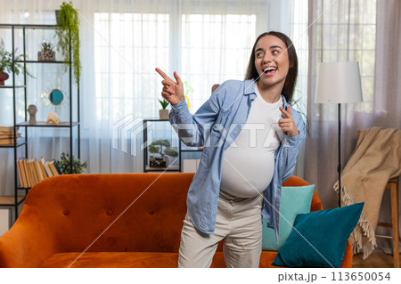 Happy smiling young pregnant woman playfully dancing listening music with big belly at home Happy smiling young pregnant woman playfully dancing listening music with big belly at home 113650054