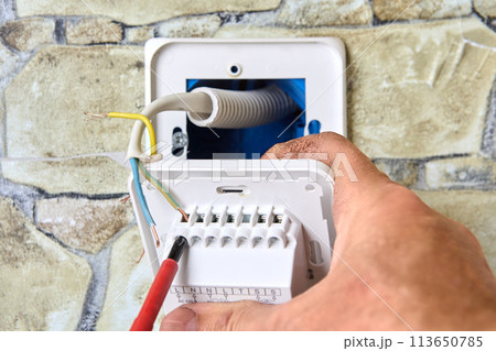Wiring new electrical socket of thermostat in stone wall, Electrician Installing, connecting live neutral and ground wires, work involved in electrical fittings. 113650785