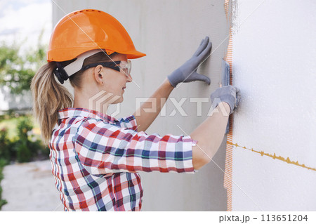 Insulation of the house with polyfoam. The worker is checking with the construction level the accuracy of the installation of polystyrene board on the facade. Insulation of the house with polyfoam. The worker is checking with the construction level the accuracy of the installation of polystyrene board on the facade. 113651204