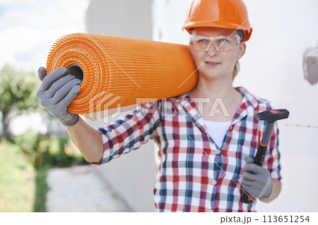 The woman with rolls of reinforcing fiberglass. Insulation of the house with polyfoam board on the facade 113651254