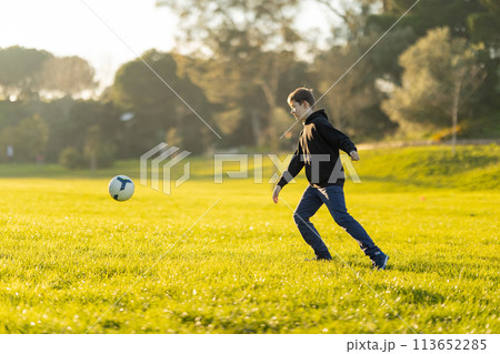 A boy kicks a soccer ball in a field 113652285