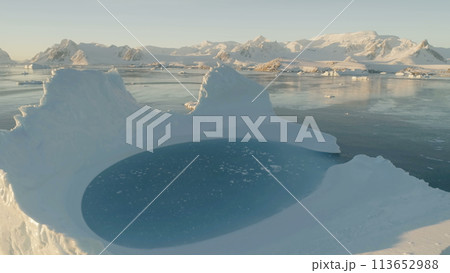 Close-up iceberg pool. Antarctica aerial view drone flight . Slow motion zoom the white iceberg with oval blue clear water pool next to the Antarctic continent. Snow covered mountains background. 113652988