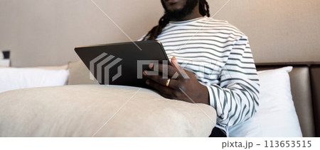 Smiling young African American man using digital tablet remote job sitting on the bed at home. concept online technology communication 113653515