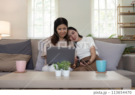 Senior mother and adult daughter relaxing and looking at laptop together at home 113654470