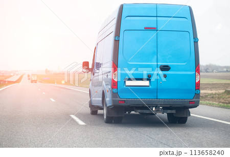 A blue manufactured goods van transports non-food cargo along a highway in the spring against the backdrop of the sun, copy space for text, industry 113658240