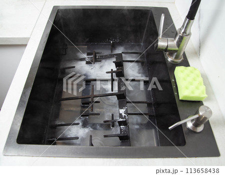 Dirty gas stove grates in the sink with a modern oxygen cleaner for kitchen cleaning. Cleaning the kitchen, removing grease stains, close-up 113658438